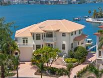 Waterfront home featuring a tile roof, manicured landscaping, private boat dock, and multi-level balconies overlooking the water at 6130 Kipps Colony W Dr, Gulfport, FL 33707