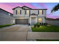 Two-story home features a well-manicured lawn, gray shutters, and a two car garage at dusk at 13227 Great Plains Dr, Riverview, FL 33579