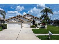 Charming single-story home featuring a well-manicured lawn, mature palm trees, and a convenient two-car garage at 1920 Folkstone Pl, Wesley Chapel, FL 33543