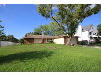 Charming single-story home with a well-maintained lawn and mature trees under a blue sky at 1670 Palmwood Dr, Clearwater, FL 33756