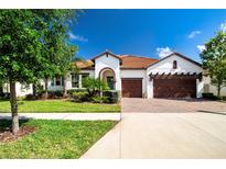 Charming single-story home with a well-manicured lawn, lush landscaping, and a brick-paved driveway at 16913 Clear Cork Dr, Wimauma, FL 33598