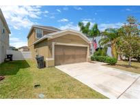 Two-story tan home with a two car garage, driveway, green lawn, and palm trees at 1210 Trailwater St, Ruskin, FL 33570
