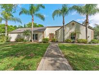 Charming single-story home with a well-manicured lawn and mature palm trees lining the walkway to the front door at 1591 Chestnut W Ct, Palm Harbor, FL 34683