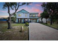 Beautifully elevated coastal home featuring a brick paved driveway, multiple balconies, and professionally landscaped yard at 1827 Venetian Point Dr, Clearwater, FL 33755