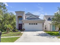 Two-story home with neutral paint, a two car garage, and tidy front yard with palm trees under a beautiful blue sky at 5634 Tanagergrove Way, Lithia, FL 33547
