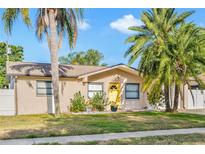 Charming single-story home with a bright yellow front door, surrounded by lush tropical landscaping and palm trees at 715 Charlotte Ave, Tarpon Springs, FL 34689