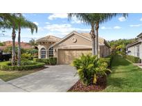 Charming home featuring a tan facade, tile roof, and lush landscaping with palm trees and manicured hedges at 14521 Mirasol Manor Ct, Tampa, FL 33626
