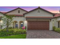 Charming home featuring a brick driveway, a two-car garage, and lush landscaping with a stucco facade and tile roof at 17228 Holly Well Ave, Wimauma, FL 33598