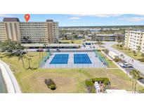 Aerial view of blue tennis courts and the building with parking spots near the grassy area under a sunny, partly cloudy sky at 4725 Cove Cir # 302, St Petersburg, FL 33708