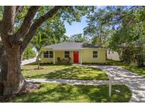 Charming yellow home featuring a bright red door, lush lawn, and mature trees at 617 Scotland St, Dunedin, FL 34698