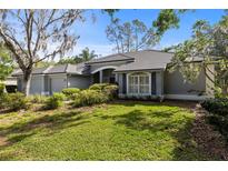 Charming single-story home with gray exterior, manicured lawn, and lush landscaping at 1003 Berkshire Ln, Tarpon Springs, FL 34688