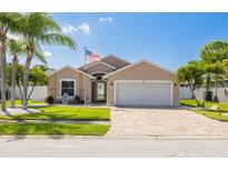 Charming home with a manicured lawn, decorative palm trees, brick driveway, and an American flag at 384 Tavernier Cir, Oldsmar, FL 34677