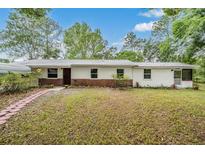 Charming single story home with a brick base, white siding, metal roof, and lush landscaping at 7249 Berry Rd, Zephyrhills, FL 33540