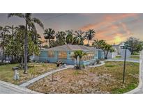 Charming light blue home featuring tropical landscaping and a welcoming pathway under a stunning colorful sunset sky at 512 79Th Ave, St Pete Beach, FL 33706