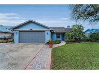 Charming light-blue house features a well-maintained lawn, brick path, and a gray two-car garage at 8742 Bermuda Ln, Port Richey, FL 34668