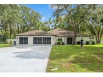 Charming single-story home featuring a well-manicured lawn, double garage, and beautiful mature shade trees at 9395 Belvedere St, Spring Hill, FL 34608