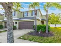 Inviting townhome featuring a two-car garage, charming landscaping, and a well-maintained lawn with palm trees at 20224 Pond Apple Ln, Tampa, FL 33647