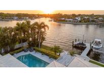 Aerial view of waterfront property featuring a pool, dock, and lush landscaping at sunset at 935 Eden Isle Ne Dr, St Petersburg, FL 33704
