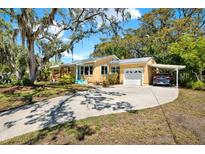 Charming, one-story yellow home with a driveway and carport nestled under large, shady trees at 2049 Broadway, Clearwater, FL 33755