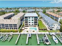 An aerial view shows a white condo building with a boat dock and pool, situated near a scenic waterfront at 455 Pinellas Bayway S # 2A, Tierra Verde, FL 33715
