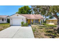 Charming single-story home features a cheerful yellow door, attached garage, and well-maintained lawn at 10819 Los Santos Dr, Port Richey, FL 34668