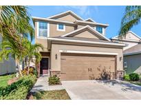 Two-story home featuring a two-car garage, stone accents and tropical landscaping at 16717 Myrtle Sand Dr, Wimauma, FL 33598