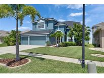 Charming blue two-story home with a well-manicured lawn, lush landscaping, and a convenient three-car garage at 1806 Mira Lago Cir, Ruskin, FL 33570