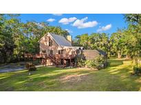 Stunning exterior view of a tan home featuring a metal roof, large deck, and screen enclosed outdoor space surrounded by lush greenery at 9298 Carr Rd, Riverview, FL 33569