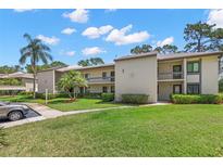 A two-story condo building showcasing a lush green lawn, palm trees, and a beige exterior on a sunny day at 135 Nina Way # 35, Oldsmar, FL 34677