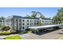 White condo building features balconies, a stone stairwell, and a covered parking area at 4801 Airport Rd # 214, Zephyrhills, FL 33542