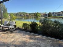 Enjoy the beautiful lake view from this gorgeous brick patio with rocking chairs and lush landscaping at 4810 Diamonds Palm Loop, Wesley Chapel, FL 33543