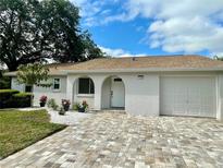 Charming home with white stucco, arched entry, brick driveway, and lush landscaping creating inviting curb appeal at 11241 Temple Ct, Seminole, FL 33772