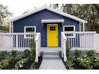 Charming blue home with bright yellow front door and lovely landscaped yard and white porch railing at 8303 N 17Th St, Tampa, FL 33604