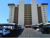 Condo building exterior showcasing balconies, covered parking, and landscaping under a clear blue sky at 15400 Gulf Blvd # 502, Madeira Beach, FL 33708