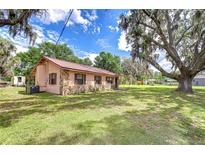 Charming single story home showcasing a unique stone facade and complemented by a lush lawn and mature trees at 8320 Purvis Rd, Lithia, FL 33547