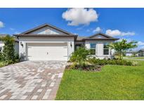 Charming single-story home featuring a manicured lawn, brick driveway, and attached two-car garage at 11447 Shoreline Trl, Parrish, FL 34219