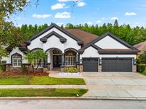 Charming stucco home featuring a three-car garage, manicured lawn, and elegant architectural details at 15045 Wind Whisper Dr, Odessa, FL 33556