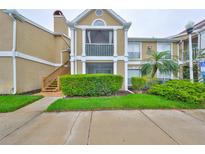 Two-story tan condo with a screened balcony, wooden staircase, and lush landscaping at 9481 Highland Oak Dr # 1206, Tampa, FL 33647