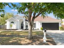 Charming white stucco home featuring a dark garage door and a well-maintained lawn with mature trees at 1608 Ledgestone Dr, Brandon, FL 33511
