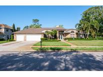 Charming brick home with a lush green lawn, manicured landscaping, and a three car garage at 2990 Eagle Estates W Cir, Clearwater, FL 33761