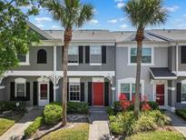 Charming townhome featuring a red door, lush landscaping, and beautiful palm trees at 273 Countryside Key Blvd, Oldsmar, FL 34677