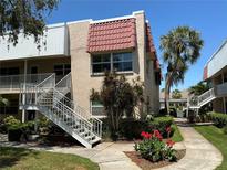 Charming condo exterior with a red tiled roof, white stairs, tropical plants and a well-manicured lawn on a sunny day at 10032 65Th N Ave # 14, St Petersburg, FL 33708