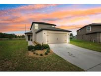 Inviting two-story home featuring a well-manicured lawn and a two-car garage under a colorful sunset at 14100 Holly Hammock Ln, Brooksville, FL 34613