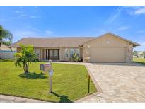 Charming single-story home boasts a well-manicured lawn, brick driveway and decorative trees under a bright blue sky at 3506 Seaway Dr, New Port Richey, FL 34652