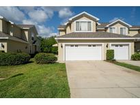 Two-story tan home featuring a white garage door, lush green landscaping, and a bright blue sky at 6507 Spring Oak Ct, Tampa, FL 33625