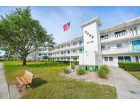 Well-maintained condo building with landscaped lawn, mature tree, bench, and American flag at 8533 110Th St # 207, Seminole, FL 33772