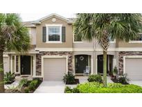 Charming townhome exterior with stone accents, a two-car garage, and tropical landscaping at 10425 Yellow Spice Ct, Riverview, FL 33578