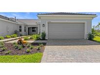 Charming home featuring a gray two-car garage, landscaped yard, and paver driveway at 27156 Capri Shores Cir, Englewood, FL 34223