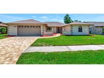 Charming single-story home boasting a manicured lawn, brick driveway, and attached two-car garage at 6056 Fall River Dr, New Port Richey, FL 34655
