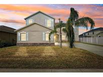 Charming two-story home with stone accents, lush lawn, and mature palm trees against a colorful sunset sky at 11907 Streambed Dr, Riverview, FL 33579